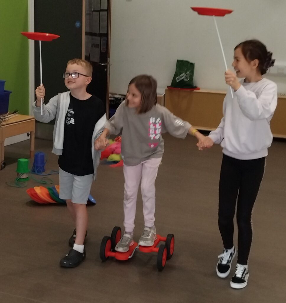 Children trying circus skills activities at summer holiday club.